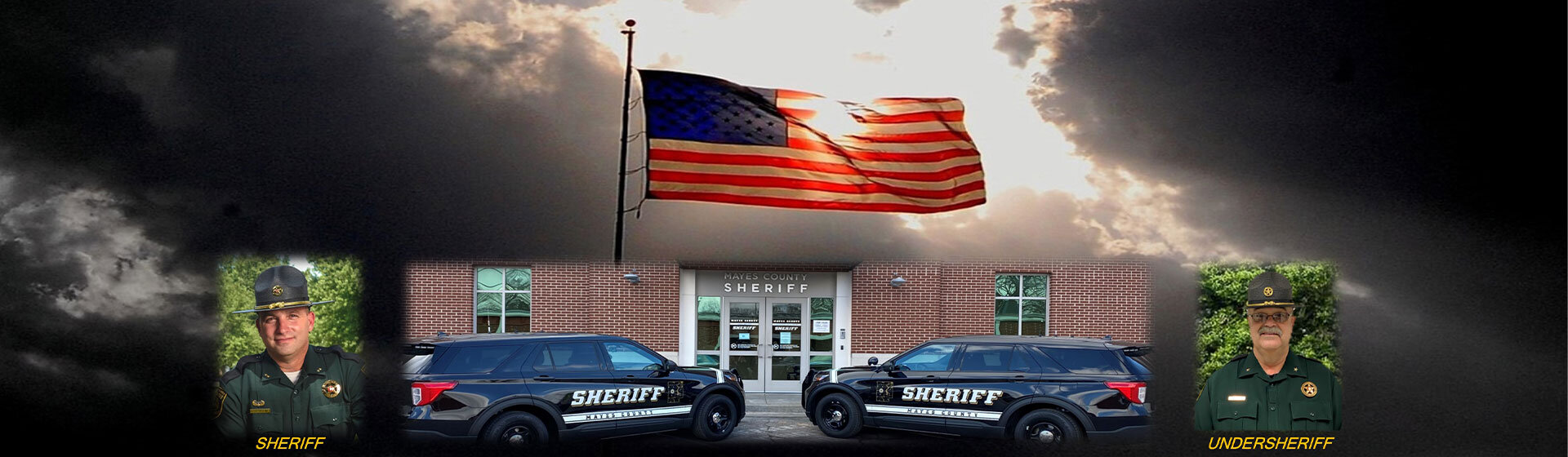 The Flag of the United States of America hovers above the sheriff's office. Two sheriff vehicles are parked on the outside.